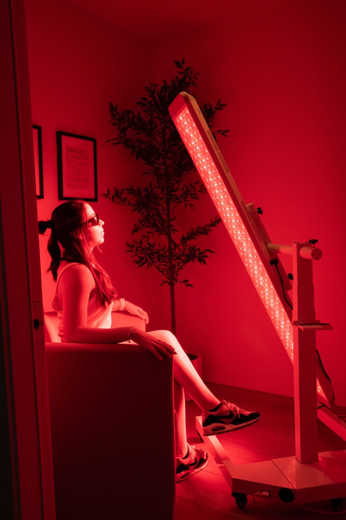 Person sitting on a couch in a room with red lighting, looking at a device.